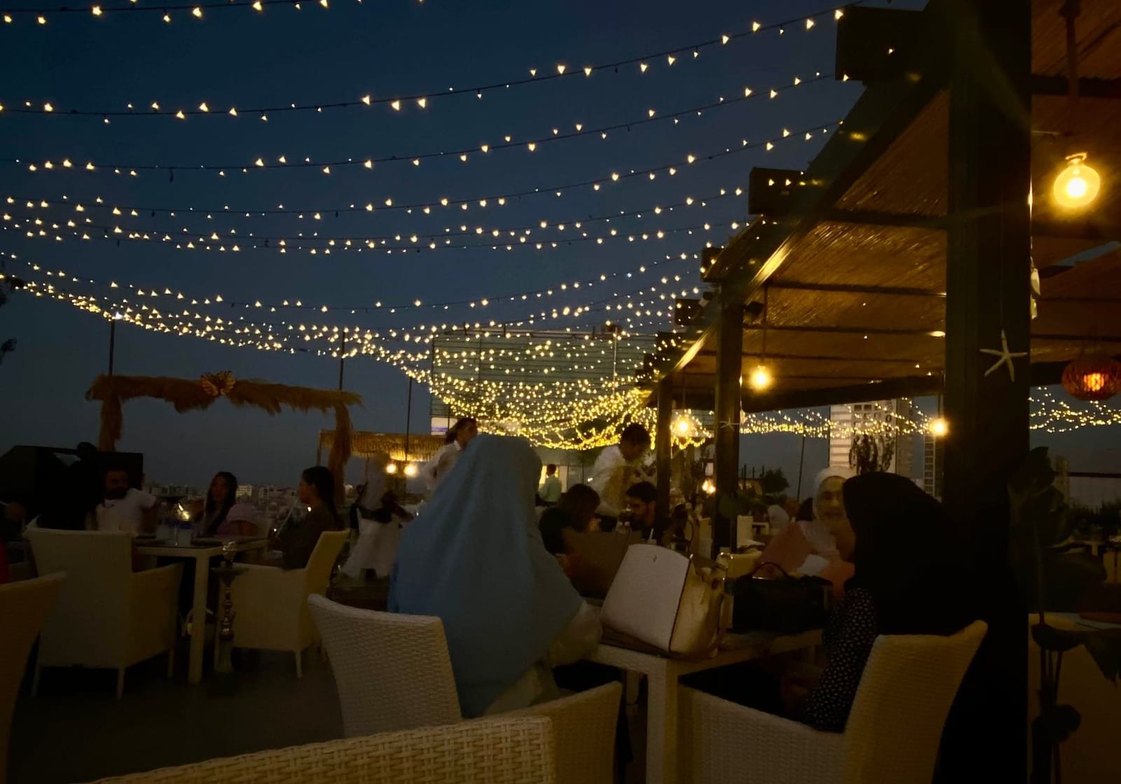 Rooftop tables under string lights at night
