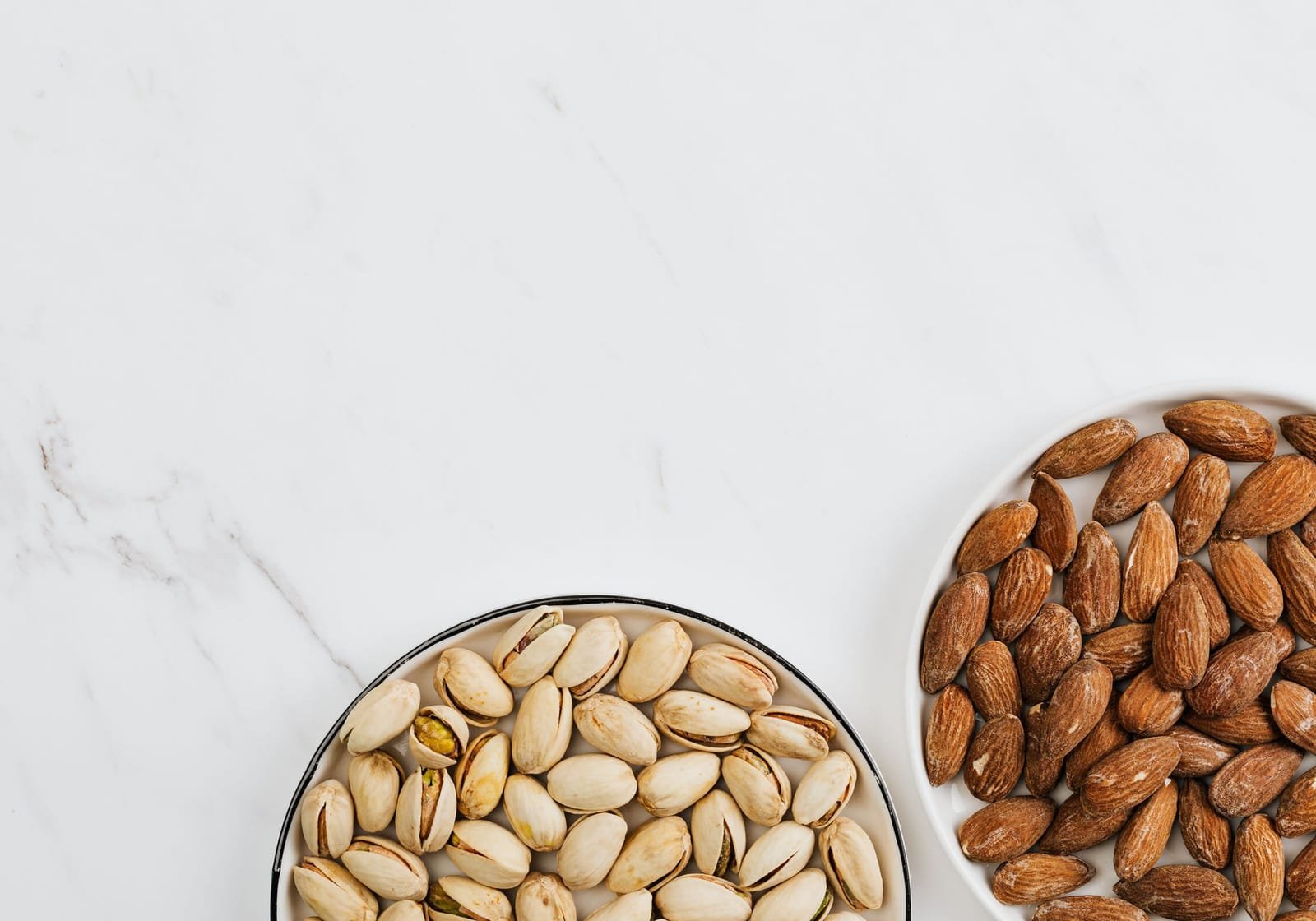 Pistachios and almonds in bowls on white marble